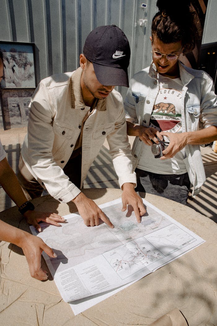 A group of friends examines a map while planning a trip outdoors under bright sunlight.